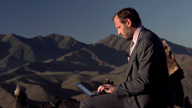 Young businessman working on laptop sitting on the trunk in the mountains
