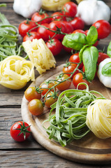 Raw pasta, tomato and basil on the wooden table