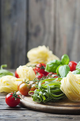 Raw pasta, tomato and basil on the wooden table