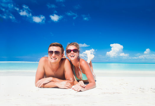 happy young caucasian couple in sunglasses lying on beach