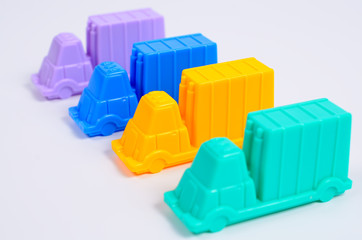Fototapeta premium Four plastic toy trucks cars of different colors on a white background. Cars are next to each other. Close up view, selective focus.