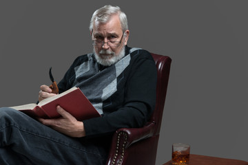 adult senior male sitting in armchair with book, pipe and drink