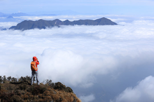 young woman hiker taking photo on mountain peak