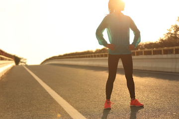 Fototapeta na wymiar fitness young woman runner standing with her hands on hips on sunrise road