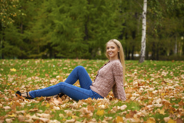 Happy beautiful woman in blue jeans sitting in the autumn park