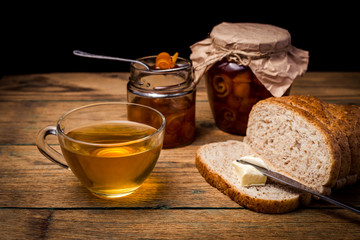 Tea and bread with orange marmalade on wooden background