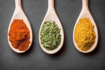 Three wooden spoons with colorful spices on black background.