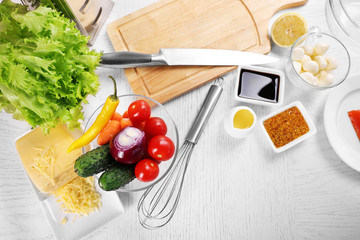 Kitchen utensils and ingredients for salad on table, on light background