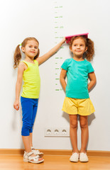 Fototapeta na wymiar Little girl help friend to measure height on scale