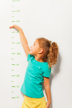 Little girl pretend how high she is on wall scale