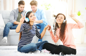 Two teenager girls listening to music with headphones in living room