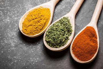 Three wooden spoons with colorful spices on black background.