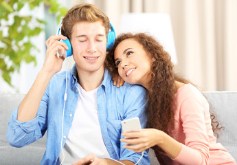 Teenager couple listening to music with mobile phone on a sofa