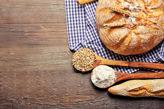 Fresh baked bread, flour, wheat in spoons and napkin on the wooden background