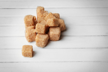 Pile of brown sugar cubes on white wooden background