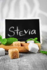 Pile of brown sugar cubes and stevia  on grey wooden background