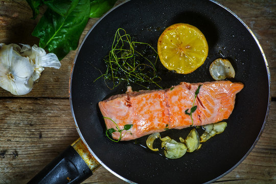 salmon fillet frying in the pan with aromatic herbs, garlic and