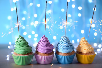 Varicolored cupcakes icing with sparklers in a row on a glitter background