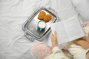 Woman in pajamas reading a book on her bed