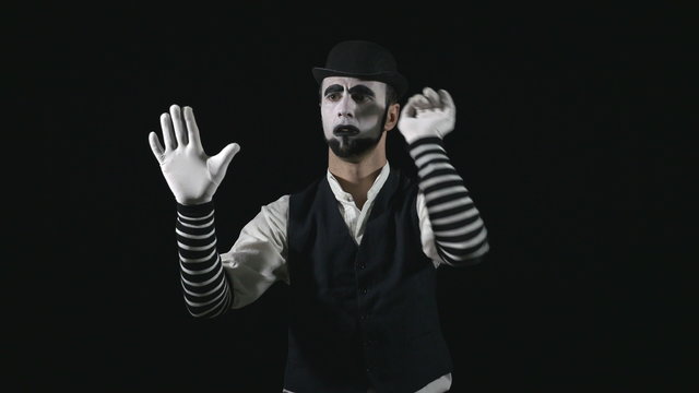 Young funny mime behind an invisible window