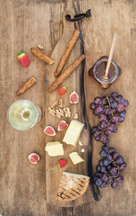 Glass of white wine, cheese board, grapes, figs, strawberries, honey and bread sticks on rustic wooden background
