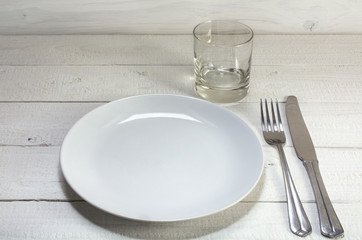 empty white plate with knife, fork and drinking glass on a white