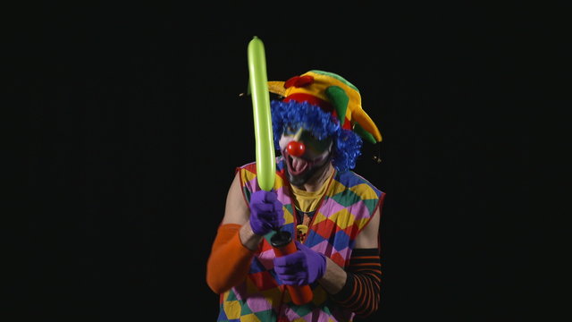 Young funny clown inflating a balloon