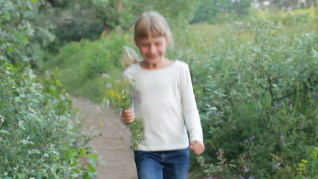 Happy little girl running and smiling at camera on the meadow, holding flowers