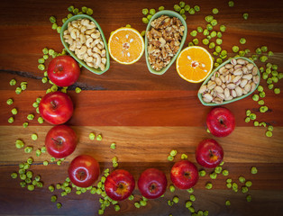 Apples, oranges, pistachios, walnuts, cashews, and wasabi peas on wooden table. Top view