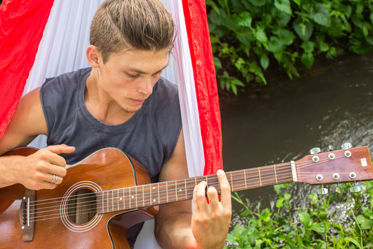 Young man composing music with a guitar in a hammock in the fore