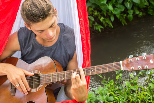 Young man composing music with a guitar in a hammock in the fore