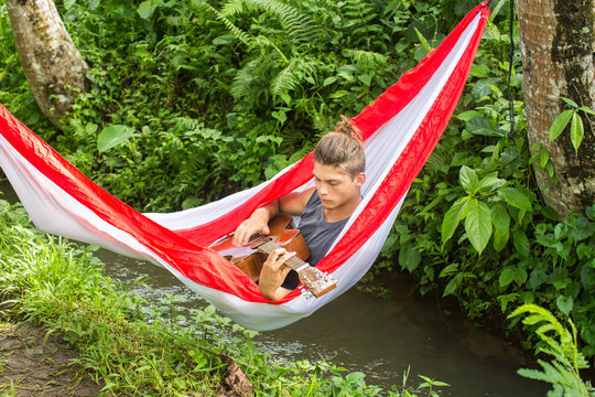 Young man composing music with a guitar in a hammock in the fore