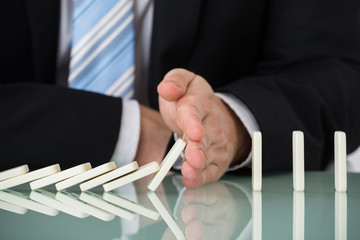 Businessperson Stopping Dominos Falling On Desk