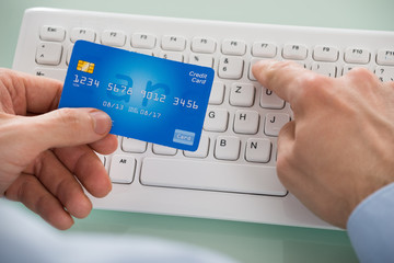 Person's Hand Holding Card While Using Keyboard