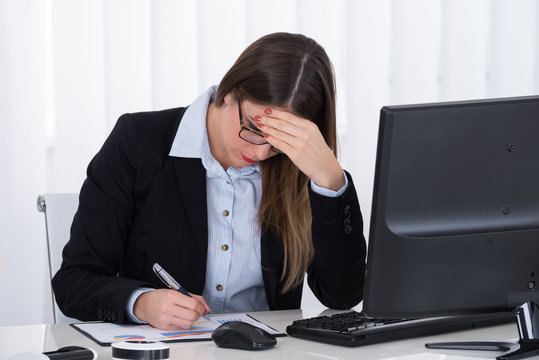 Stressed Businesswoman Sitting At Desk With Financial Report