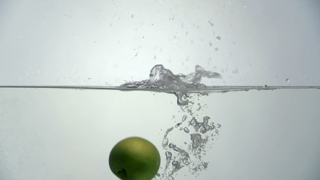 Close up of ripe green apple falling into water against white background in slow motion