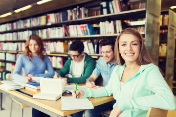 happy student girl writing to notebook in library