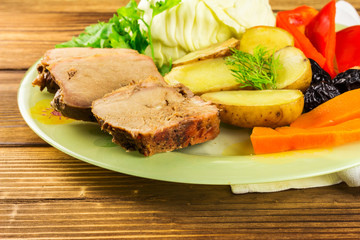 Healthy food, sliced pork meat with stewed various vegetables in plate, on wooden background, close-up view