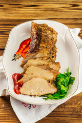 Sliced pork meat with parsley and tomato sauce in plate on napkin, wooden background