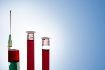 Syringe and two vials of blood on blue background