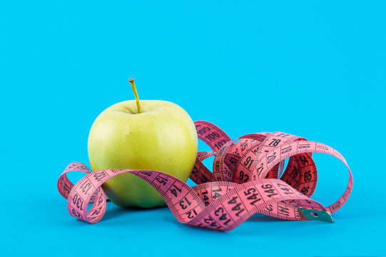 Green apple and red measuring tape on a blue background