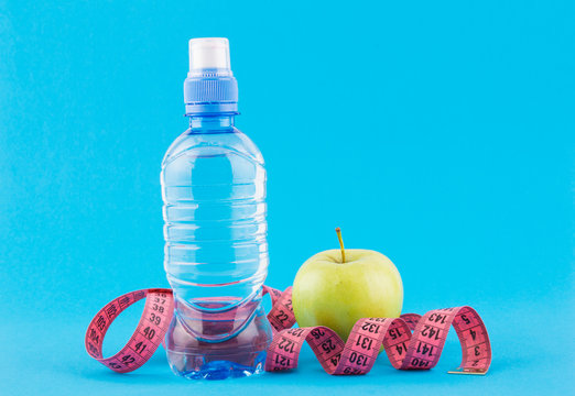 Green apple, bottle of water, measuring tape on a blue background