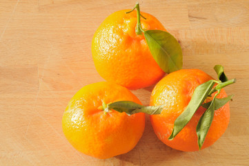 Tre clementini con le loro foglie verdi, su un tavolo di legno, vista dall'alto, luce solare