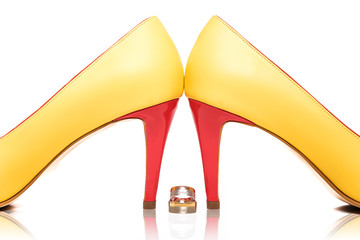 Wedding rings with the event date engraved on them besides unusual modern multicolor bridal shoes against white background with reflection and copy space
