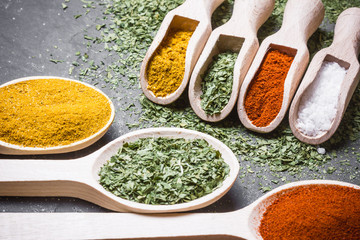 Wooden spoons with colorful spices on black background.