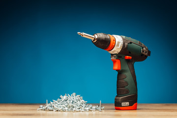 cordless screwdriver and fasteners screws on blue background