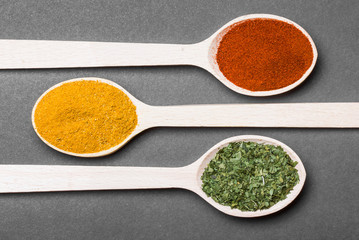 Three wooden spoons with colorful spices on black background.