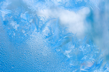 Fototapeta na wymiar Slightly blurred beautiful frost pattern and drops of water on a window glass (as an abstract winter background)