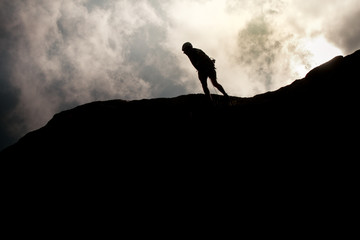 Man walking on the top of a hill after climbing with clouds in backrgound.