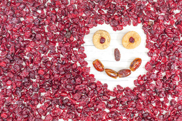 Funny face made of dried fruits on white wooden background